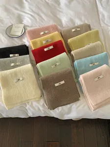Detailed close-up of soft knitted scarves in various solid pastel colors on white bedding