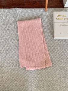 Detail view of a minimalist pink ribbed knit winter scarf on a grey textured rug