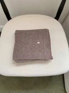 Detailed view of a brown ribbed knit scarf featuring a metal tag on a white chair