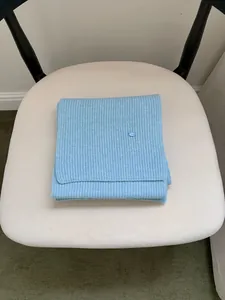 Detail shot of a neatly folded light blue ribbed knit scarf with metal tag on a chair.