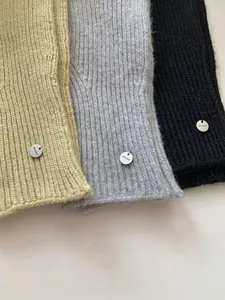 Detail view of knitted arm warmers in green, grey, and black with simnice metal tags.