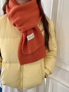 Primo piano di una sciarpa di lana arancione abbinata a un piumino giallo pallido