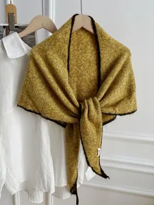 Detalle de chal de punto de lana amarillo mostaza con borde de contraste oscuro en camisa.