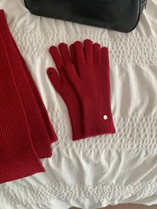 Close-up of red ribbed knit gloves and scarf set for winter on white textured surface.