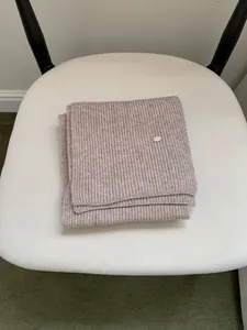 Detail view of the oatmeal-colored ribbed scarf with a small metal logo tag.