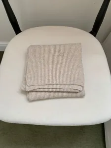 Detailed view of a beige ribbed knit scarf with a small metal tag on a white chair.