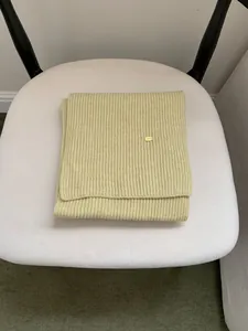 Close-up of a pale green ribbed knit scarf with a small gold metallic logo tag.