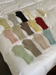 Detailed view of various colors of knitted winter gloves with small metal tags for women.
