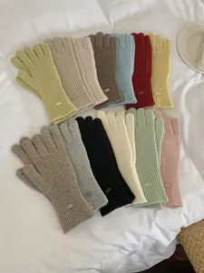 Collection of colorful ribbed knit gloves with decorative metal labels in various soft tones.