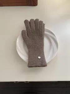 Soft brown knitted winter wool glove with silver brand tag on a white ceramic plate