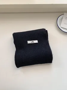 Cozy minimalist black knitted wool scarf with a white label for winter gift set.
