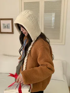 Side view of a woman wearing a cozy cream knitted hooded hat with braided ties