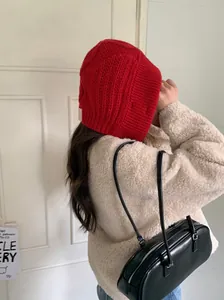 Close-up side view of a cozy red knitted earflap hood hat worn by a model indoors