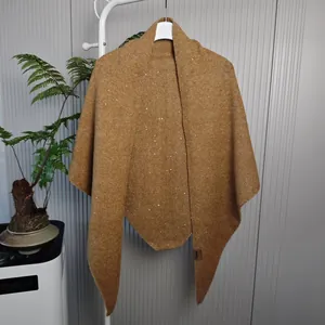 Detail van een gemberkleurige gebreide sjaal met pailletten van een wolmix aan een rek.