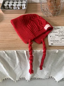 Close-up of a red knitted trapper hat with long braided tassels on a wooden table