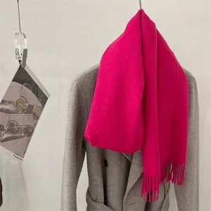 Détail d'une écharpe en laine fuchsia vibrante avec franges sur un manteau gris élégant.