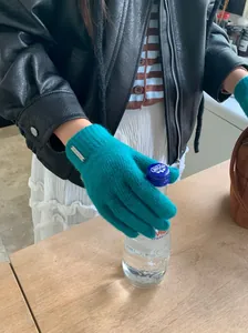 Nahaufnahme einer Person mit blaugrünen Strickhandschuhen aus Wollmischung und Metallemblem