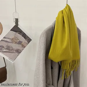 Détail d'une écharpe en laine épaisse vert citron avec des franges sur un manteau gris