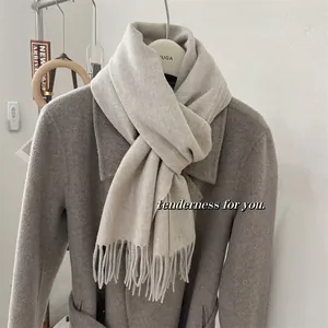 Gros plan d'une écharpe beige en 100% laine avec des franges drapée sur un manteau.