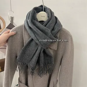Gros plan d'une écharpe en laine grise unie avec des franges sur un manteau de couleur beige.