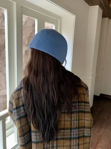 Back view of a woman wearing a soft blue knitted beanie in a cozy indoor setting.
