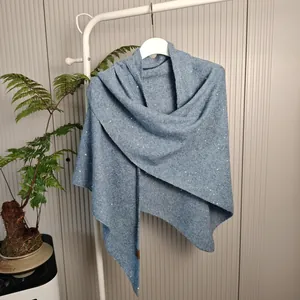 Blauwe gebreide wollen sjaal met pailletten detail, hangend aan een wit kledingrekje.