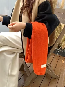 Detailopname van een feloranje gebreide wintersjaal met een wit merklabel erop