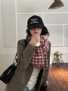 Fashionable Asian model wearing a red and beige checkered knitted scarf in a cozy cafe.
