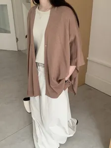 Dettaglio di un cardigan a scialle in maglia retrò marrone abbinato a una gonna bianca.