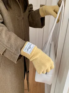 Detail view of cozy yellow knitted winter gloves with aesthetic white label and brown coat