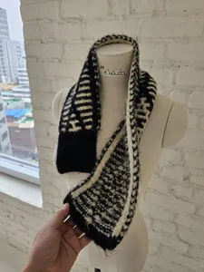 Detail view of a black and white striped knit cross muffler scarf shown on a white mannequin torso.