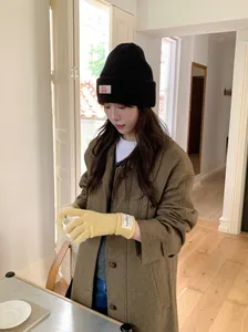 Woman wearing yellow knitted gloves and a black beanie in a cozy indoor setting