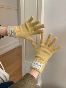 Close-up detail of yellow knitted winter gloves featuring a stylish decorative woven label