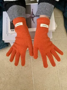 Detailed macro view of orange knit merino wool gloves with authentic 100% wool label