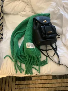 Close-up of green UNDERSON wool scarf with fringe and brand label on white bedding