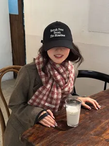 Close-up of a soft red checkered knit scarf styled with a cap in a cozy cafe setting