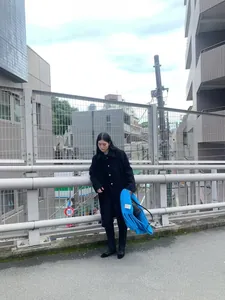 Model wearing a blue wool scarf with fringes and black coat on an urban street.
