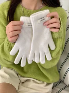Detail view of white 100% wool knitted gloves held by a model in a green sweater.