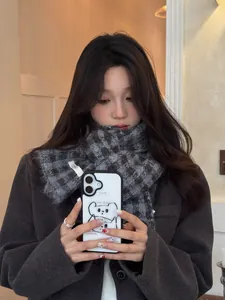 Close-up of a cozy grey checkered knitted scarf worn by a model in a warm indoor setting.
