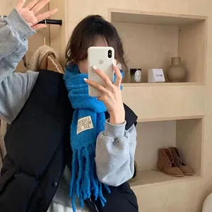 Cozy blue thick wool-feel scarf with fringes and Underson patch shown in a mirror selfie