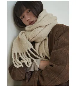 Detailed view of a thick beige wool-blend scarf with fringe tassels worn by a model