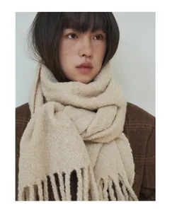 Detailed view of a thick beige wool blend scarf with long fringe tassels on a model