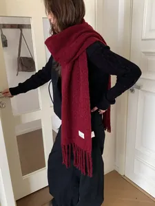 Close-up detail of a thick burgundy wool scarf featuring long fringes and white brand tag