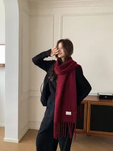 Detailed view of a soft burgundy wool scarf with tassels worn by an Asian model indoors.