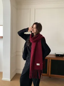 Lifestyle shot of an Asian model wearing a burgundy knitted wool scarf with tassels.