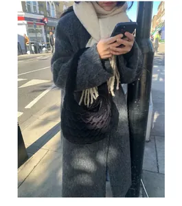 Close-up of a thick white wool scarf with fringe detail and a black quilted heart pattern bag.