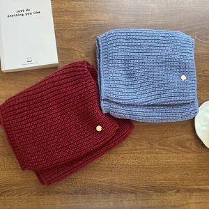 Two knitted neck warmers in red and blue with metal tags on a wooden table.
