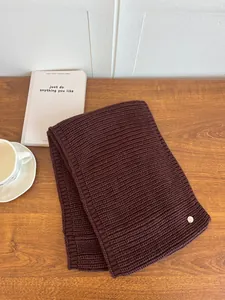 Close-up detail of a thick brown knitted neck warmer with a circular metallic tag.
