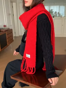 Detail view of a bright red wool blend fringe scarf worn with a black sweater