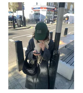 Street style view of a beige thick wool scarf with fringes and a green cap.